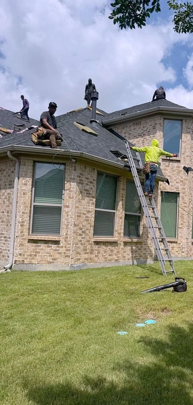 A roofing crew working on a two-story brick home, with a ladder at the eaves