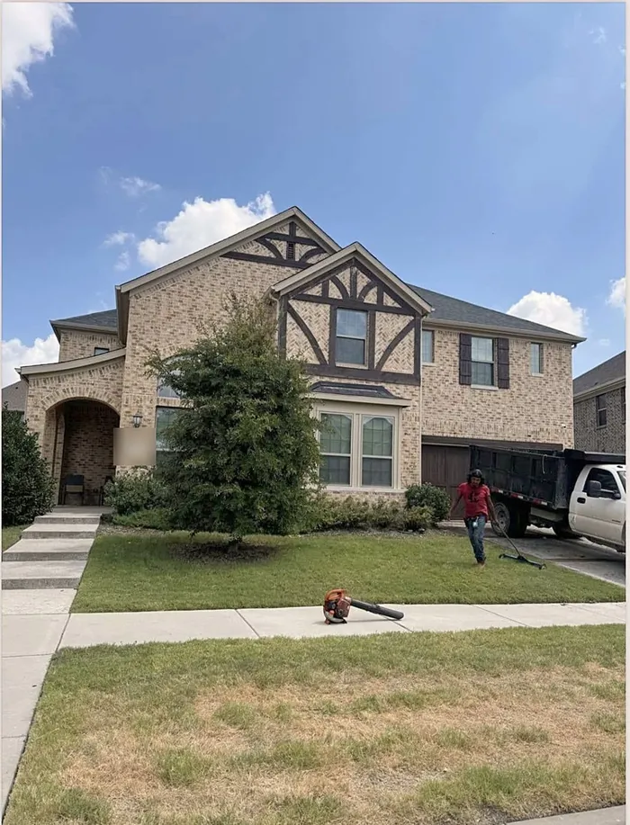 A two-story brick home after a roof replacement, with the crew cleaning up the yard