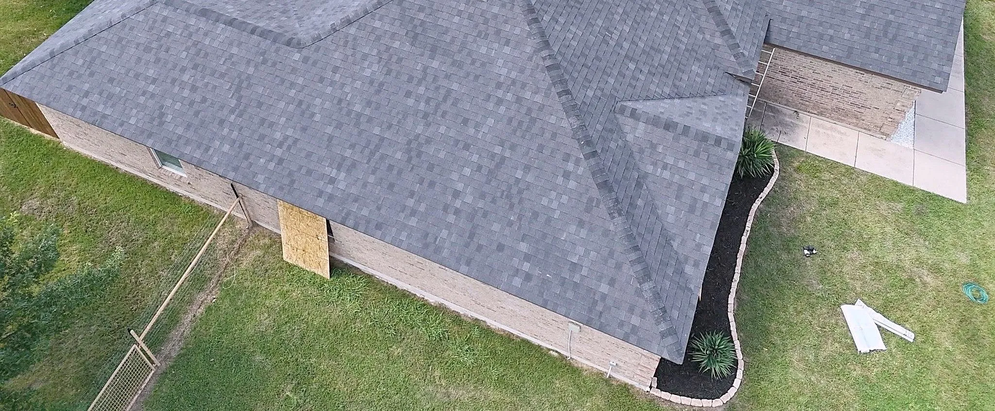 Drone view of a finished dark gray shingle roof on a brick ranch home