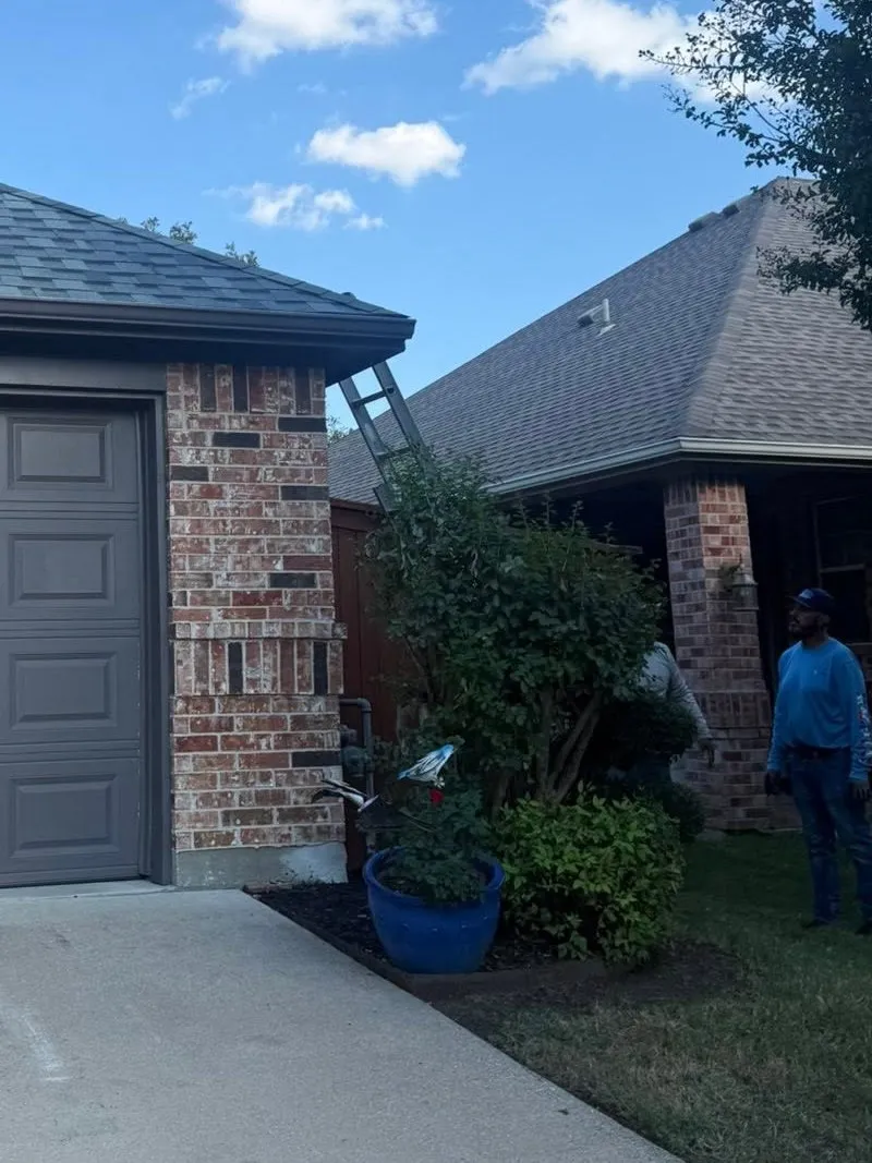 A ladder against the gutter line of a brick home while a crew member looks up at the eave