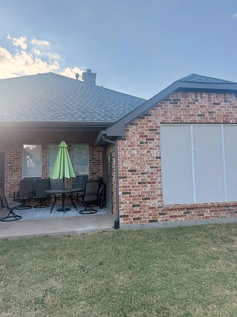 The back of a brick home with a new shingle roof, gutters and a downspout