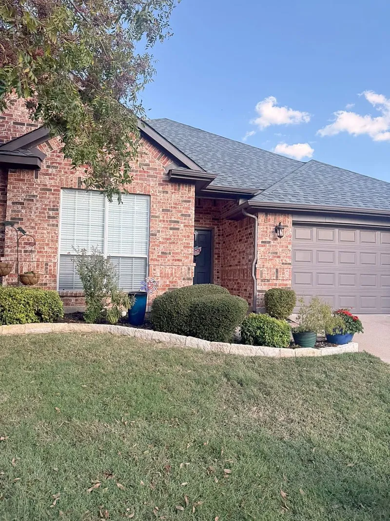A red brick home with a gray shingle roof over the front porch and garage